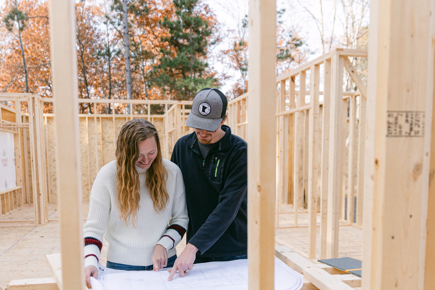 Two people reviewing building plans inside a framed house